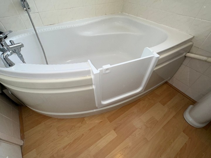 A UDOOR® bathtub door fitted into a customer's corner bath, showing the low step-through opening